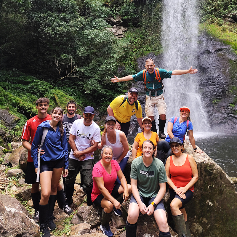 Grupo conduzido pelo Guia de Caraá pelo Sul posando em frente à Cascata Perfumada, em Caraá.